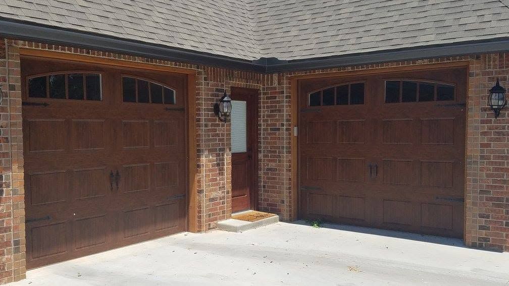 Two wood-look carriage-style garage doors with arched windows on a brick home