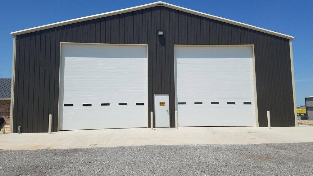 Two tall white shop doors with window rows on a dark metal building